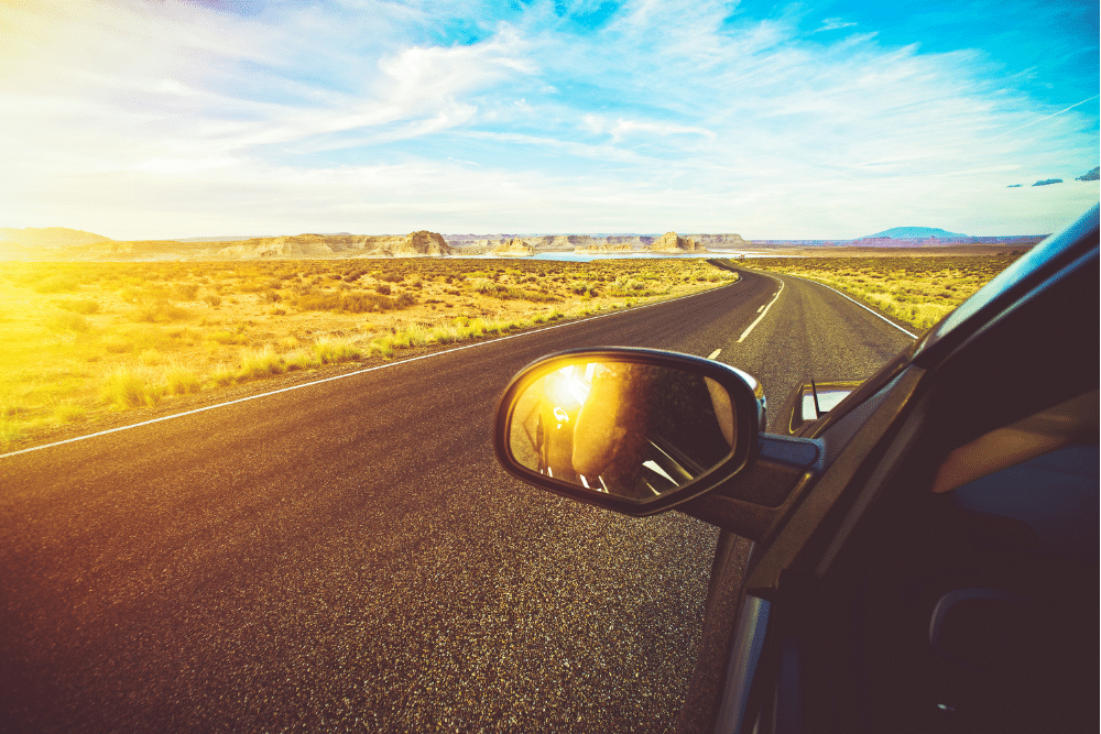 auto maintenance tips, auto repair in Arcata, CA at North Bay Automotive. Side mirror view of a car driving on a sunny open desert highway, symbolizing summer travel and vehicle performance in hot conditions.