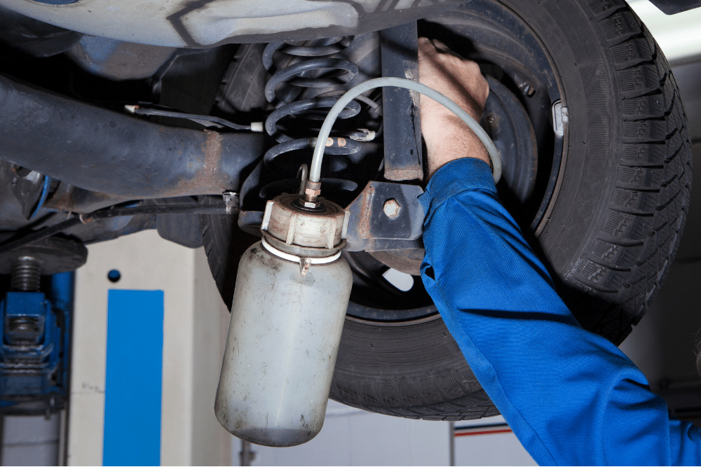 brake fluid flush, auto repair in Arcata, CA at North Bay Automotive. Mechanic bleeding brake fluid from the rear brake assembly of a vehicle using a vacuum bleeder bottle.
