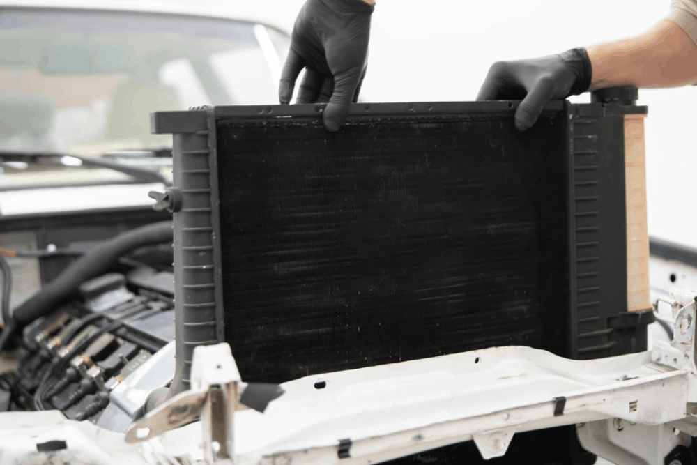 Why Radiator Service Is Essential for Summer Vehicle Reliability in Arcata -North Bay Automotive - A person wearing black gloves carefully removes a large car radiator from the engine compartment, showcasing a repair process in a clean, well-lit garage.